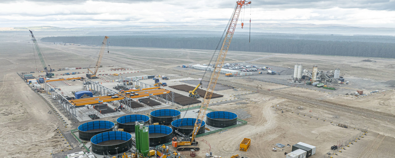 Aerial view of port buildings and storage facilities under construction in the foreground, looking out towards the sea in the distance