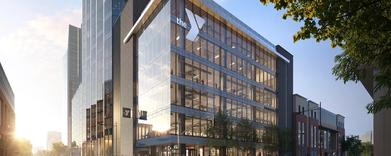 A striking glass building with the YMCA logo and sunset in the background. 