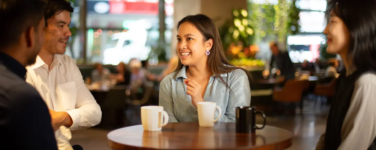 Group of colleagues sitting together having a conversation, gathered around a table with coffee mugs.