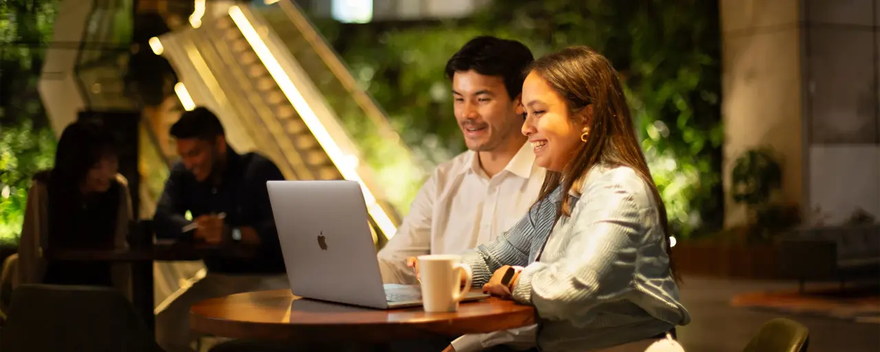 Two colleagues sitting together looking at a laptop in a plant-filled office.