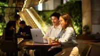 Two colleagues sitting together looking at a laptop in a plant-filled office.