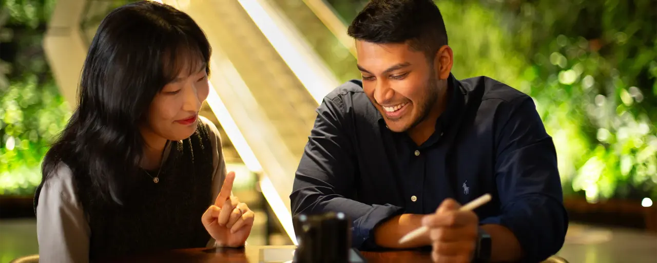 Two colleagues sitting together looking at a tablet in a plant-filled office.