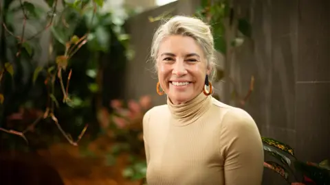 Portrait of Beth Schultz, Director of Energy and Natural Resources, ESG and Sustainability, Australia, standing outside by leafs, in yellow top, smiling.