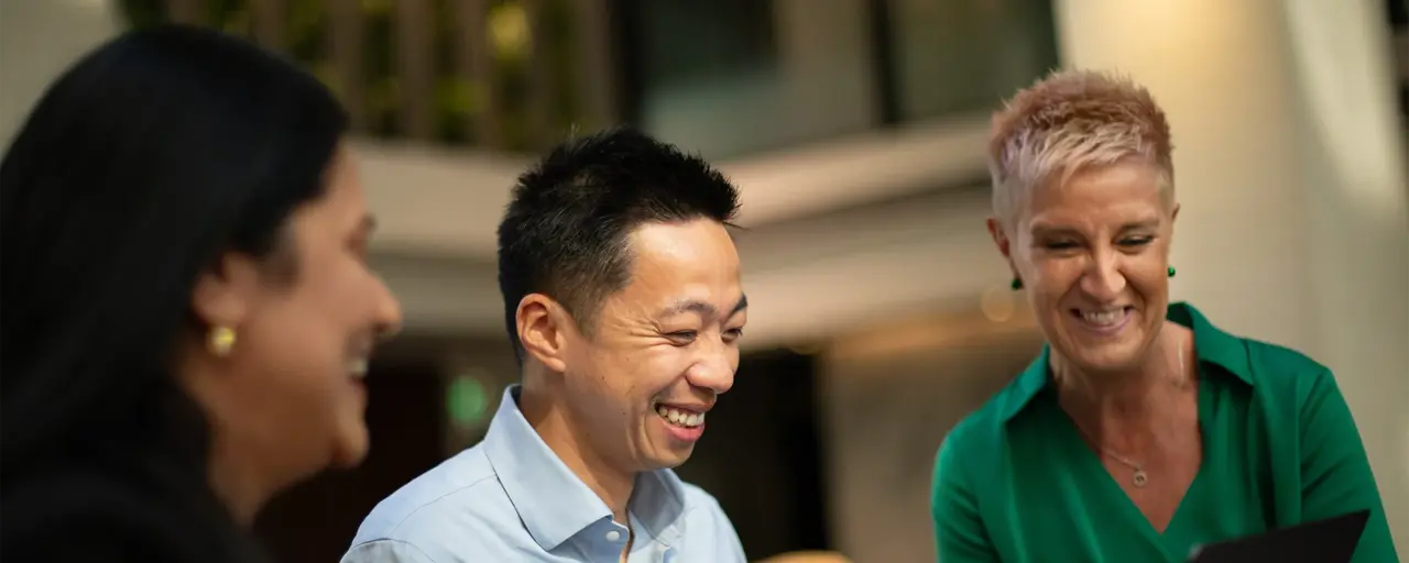 Three colleague gathered around a laptop laughing and engaging in conversation.