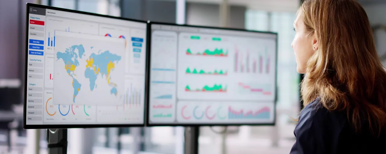 Woman looking at two screens displaying graphs