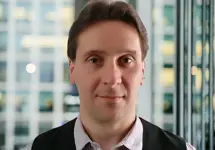 Portrait of Alistair Robson, Project Director, with city landscape featuring building with lots of windows in the background.