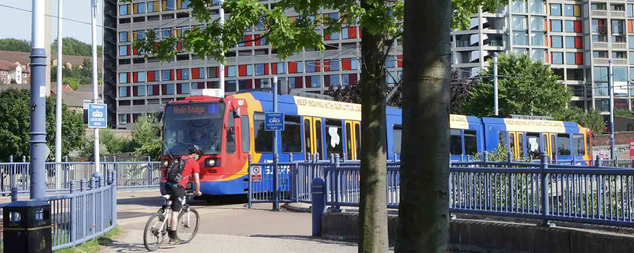 Colourful red blue and yellow tram passing through as man in red on a bike rides past