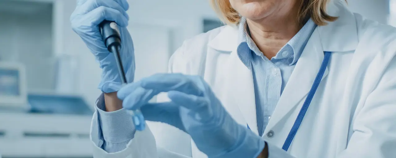 Close-up photo of a life sciences laboratory worker dressed in personal protective equipment holding specialised tools