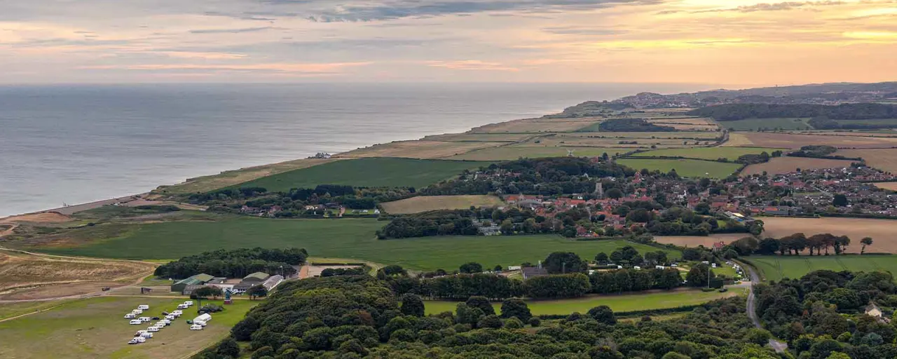 Aerial view of a coastal village with housing and fields in the foreground and the ocean in the distance