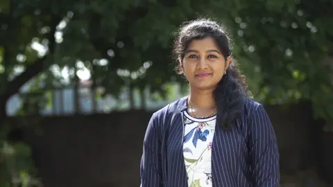 Portrait of Ashwini Dharmarajan, Senior Project Manager, Toronto, outside in front of trees.