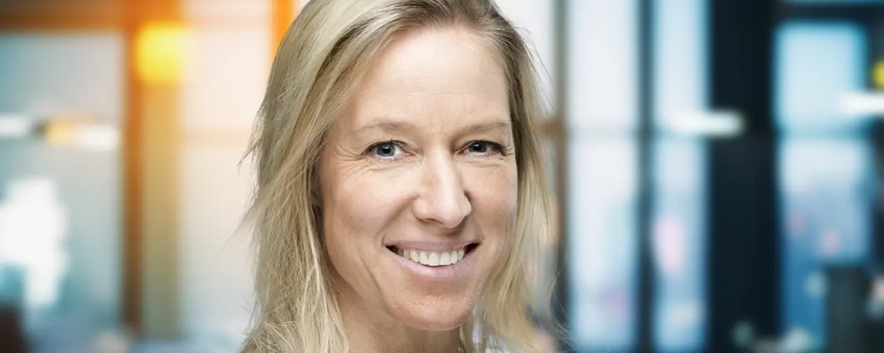 Portrait of Bettina Würfel, managing director, Germany and Austria, smiling in white shirt against office background with sunshine shinning through window.