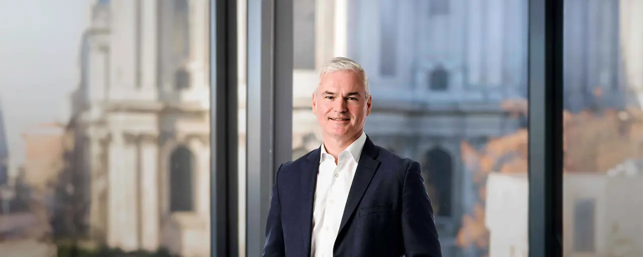 Vincent Clancy standing in the London office with the London city view in the background