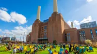 Group of people sitting outside in deck chairs in front of Battersea Power Station on a sunny day