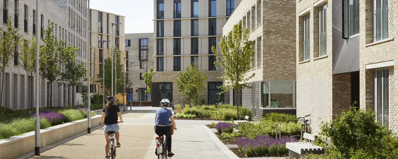 Daytime photo of a multi-storey residential development with two cyclists at the centre of the image, riding between buildings