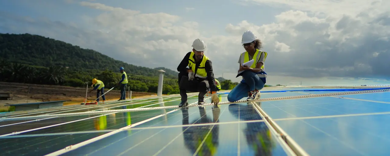 Team contractor, male engineer and female technicians wearing safety uniform, talking about installing plan, check the working system and maintenance solar panel of solar power plant to produce electricity on the roof of factory building. Industrial of renewable energy. Power generation from solar energy.