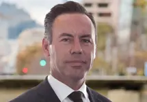 David Smith, Qatar Country Manager, standing outside featuring an urban cityscape with tall buildings and a mix of architectural styles. The scene includes some trees with autumn foliage, adding a touch of color. 