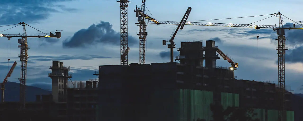 View of a hub with construction cranes surrounding the hub with dark skies.