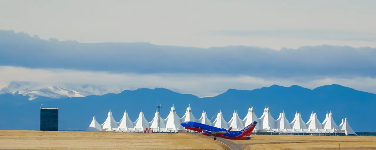  A blue and red aeroplane just taking off from the runway against a backdrop of the airport and snowcapped mountains. 