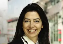 Portrait of Diana Unterstrasser, Director, Europe, Occupier and Retail, standing outside in front of buildings featuring an urban cityscape with a mix of architectural styles. The scene includes some windows and red features, adding a touch of color.