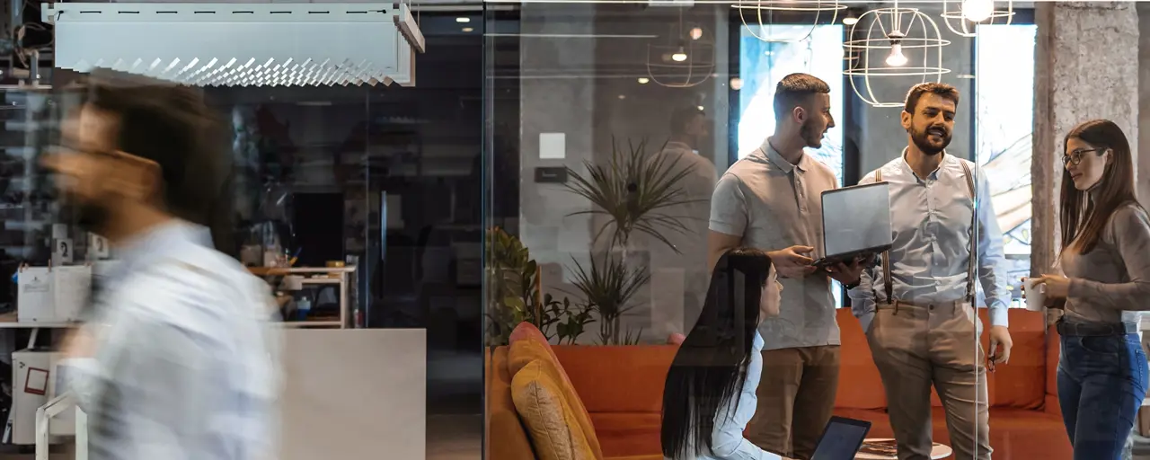 Colleagues standing around in a colorful based office, engaged in a conversation.