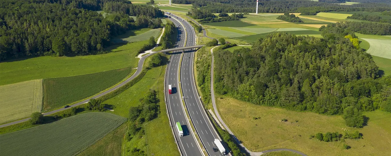 Traffic on a motorway surrounded by green fields, forest and wind turbines in the far distance