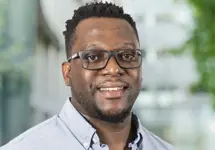 Gerald Madondo, Country Director, standing outside in front of an outdoor urban setting, featuring modern architectural elements with clean lines. There are hints of greenery, suggesting some trees or plants.