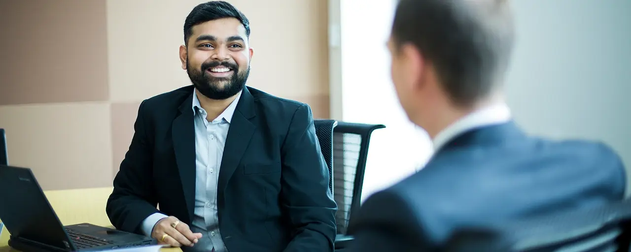 Two men sitting at a desk talking and smiling