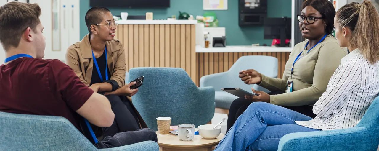 Four hospital workers sitting on blue chairs in a meeting 