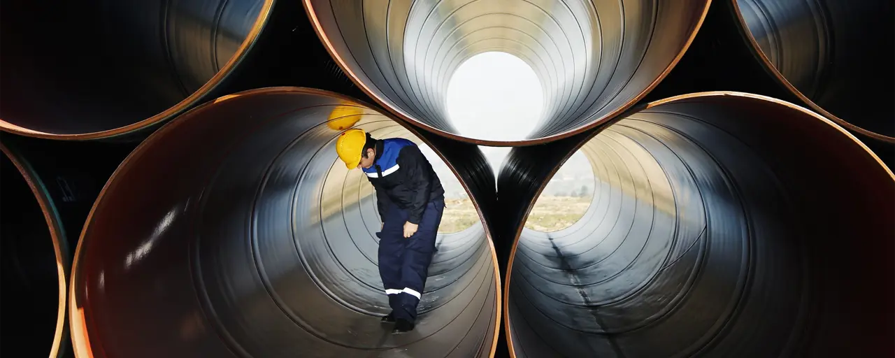 Man with yellow hard hat standing inside large cylinder 