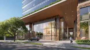 Entrance to a modern, glass building with a tree in the foreground on a sunny day