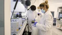 Students in a university science lab with white coats and face masks on working on machine.