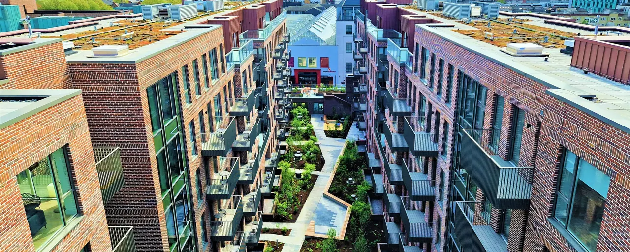 An aerial shot of a cluster of modern flats, with blue skies and small gardens. 