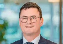 Portrait of Marc Hopman, Director, with plant based office setting with glass window in the background.