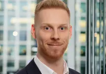 Portrait of Matt Lowe, Principal Consultant, with city landscape featuring building with lots of windows in the background.