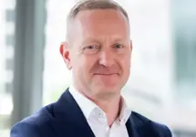 Portrait of Neil Bullen, Global Managing Director, Real Estate, In office standing by plant with his arms crossed.