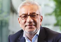 Nitesh Patel, Lead Economist, UK, standing outside in front of an outdoor urban setting, featuring modern architectural elements with clean lines. There are hints of greenery, suggesting some trees or plants.