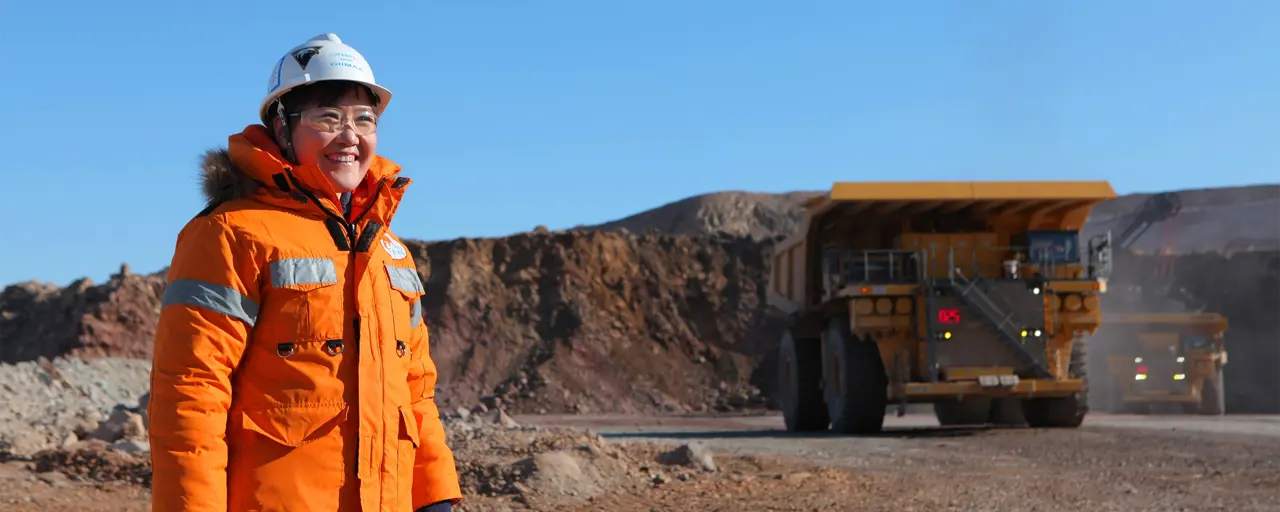 Woman standing in sandy construction site wearing orange hi vis and helmet