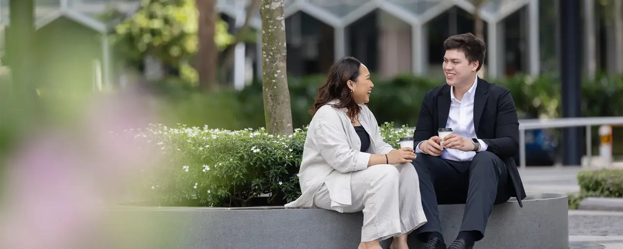 Male and female colleague sitting outside having a conversation surrounded by plants.