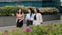 Group of three female colleagues walking and having a conversation outside surrounded by plants.