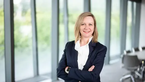 Patricia Moore, Managing Director, UK, smiling in an office with large windows and views of trees