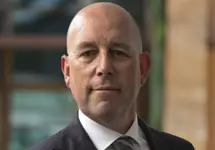 Portrait of Philip Matthews, Managing Director, Ireland, outside in front of a blurred brown background featuring a building and mix of natural and urban elements.