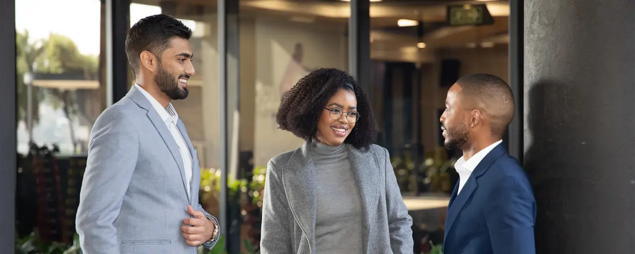 Three colleagues in plant-filled office space standing and engaging in conversation.