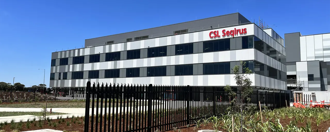 A CSL Seqirus vaccine facility, a multi-storey building set against a blue sky. 