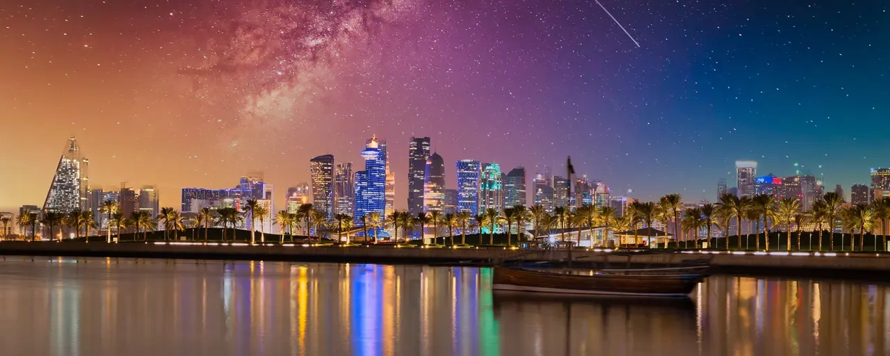 Colourful night sky above high rise buildings beside water and palm trees