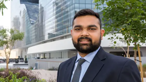 Portrait of Ranjeet Pundlik, Associate Director, Project Management, Dubai, outside in front of tall city building with glass windows.