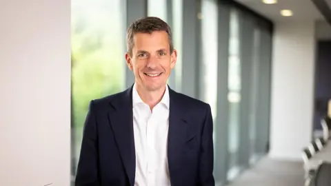 Finance Director, Richard Peers, smiling in an office interior in front of a window with trees