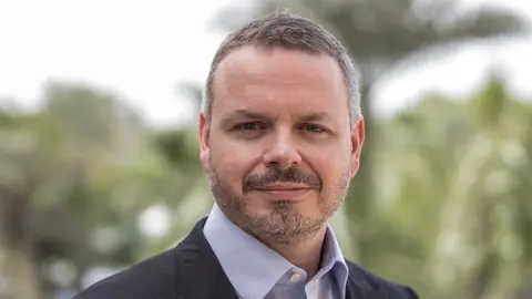 Portrait of Ryan Shalabi, Middle East Expert Lead, outside in front of blurry green scenery and trees.