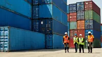 Four people in hi-vis jackets and helmets walk through a shipping container yard