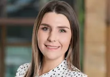 Tiffany Emmett, Construction Economist, outside in front of a blurred brown background featuring a building and mix of natural and urban elements.