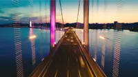 View from a bridge suspended over water at dusk with city lights in the distance